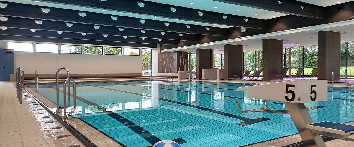 Innenaufnahme des leeren Jurabads mit Becken mit strahlend blauem Wasser. Ein Wasserball liegt dekorativ im Vordergrund.