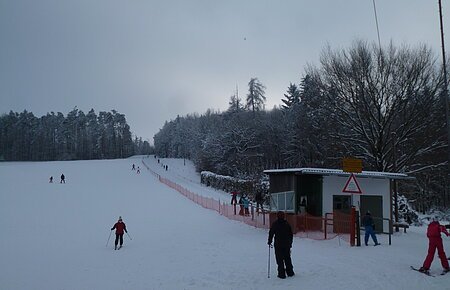 Schlepplift "Kaiserschachen" in Übersfeld Skifahrer auf einer schneebedeckten Piste neben einem kleinen Schlepplift und einem Wald im Hintergrund.