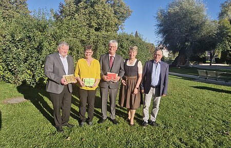 Verabschiedung Rentner 2025 Both Margit, Mayer Alfred, Josef Nuber Fünf Personen stehen auf einer Wiese vor Bäumen, drei halten bunte Geschenke in den Händen, im Hintergrund blauer Himmel. Renteneintritt der drei langjährigen Mitarbeiter der VG Monheim.