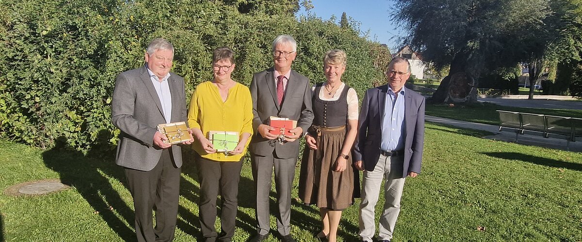 Verabschiedung Rentner 2025 Both Margit, Mayer Alfred, Josef Nuber Fünf Personen stehen auf einer Wiese vor Bäumen, drei halten bunte Geschenke in den Händen, im Hintergrund blauer Himmel. Renteneintritt der drei langjährigen Mitarbeiter der VG Monheim.