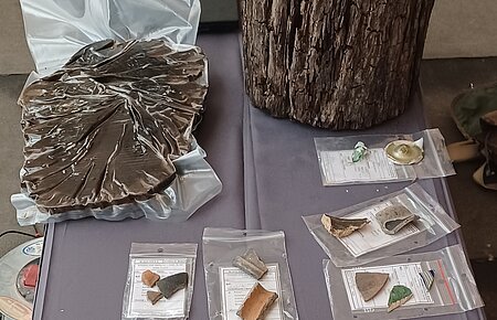 Funde der Ausgrabungen in Monheim im Hof hinter "Das Hotel by Ferber" Verschiedene archäologische Funde eingepackt in Plastiktüten auf einem Tisch ausgelegt, darunter Holzstücke und Proben in kleinen Fläschchen.