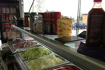 Bild einer Auslagen in einem Bistro mit Salat-Beilagen wie Tomaten, Zwiebeln, Salat, und geschnittenem Käse. Weitere Zutaten oben auf der Auslagefläche wie Saucen und Getränke links im Hintergrund.