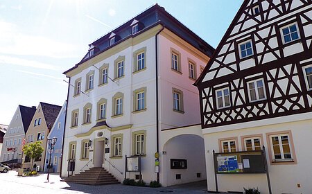 Straßenansicht der Monheimer Innenstadt: Im Vordergrund das Rathaus der Stadt Monheim, mit weiteren mehreren Gebäuden, darunter ein Fachwerkhaus, das man Schindlerhaus nennt.