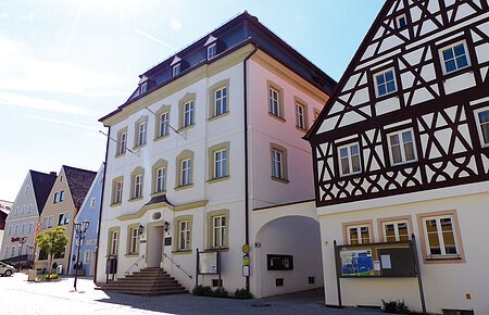 Das Rathaus der Drei-Stämme-Stadt Monheim Straßenansicht der Monheimer Innenstadt: Im Vordergrund das Rathaus der Stadt Monheim, mit weiteren mehreren Gebäuden, darunter ein Fachwerkhaus, das man Schindlerhaus nennt.