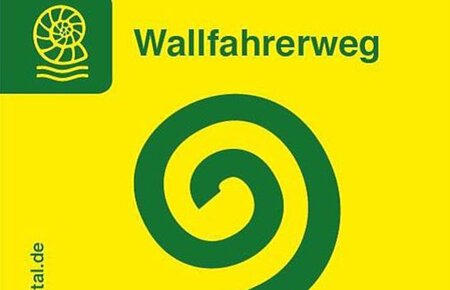 Leuchtend gelbes Wallfahrerweg-Schild: darauf mittig ein grünes Spiralsymbol mit Schrift „Wallfahrerweg“ oberhalb. Links daneben das Symbol eines Schneckenfossils. Vom unteren Eck links vertikal hoch die Nennung der Website "www.naturpark-altmuehltal.de"