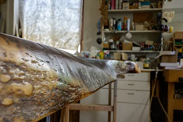 Nahaufnahme einer unregelmäßig geformten dunklen Holzoberfläche eines Tisches in einer Werkstatt mit Regalen und Werkzeugen im Hintergrund.