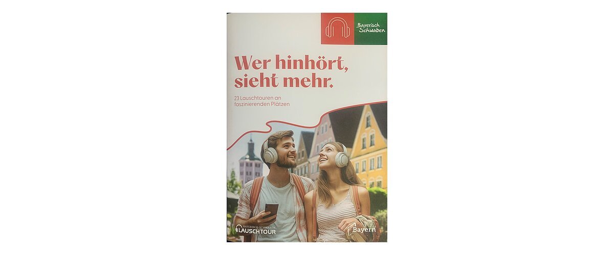 Titelblatt der Broschüre "Wer hinhört, sieht mehr" zu Lauschtouren vom Tourismusverband Allgäu/Bayerisch-Schwaben e.V.. Auf dem Foto zwei junge Personen mit hellen Kopfhörern und Rucksäcken vor bunten Häusern in einer Stadt in Bayern. Auf dem Foto der Text "23 Lauschtouren an faszinierenden Plätzen".