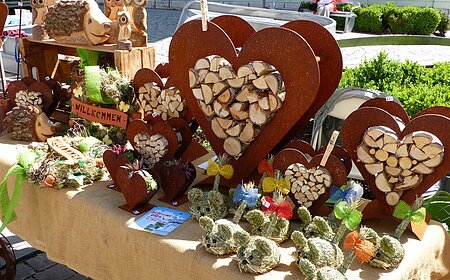 Handwerkskunst auf einem Marktstand: Herzförmige Holzdekorationen und Figuren aus Naturmaterialien auf einem Tisch.
