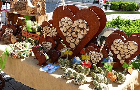 Handwerkskunst auf einem Marktstand: Herzförmige Holzdekorationen und Figuren aus Naturmaterialien auf einem Tisch.