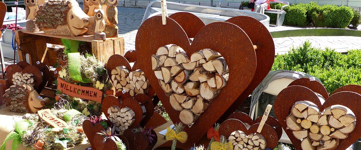 Handwerkskunst auf einem Marktstand: Herzförmige Holzdekorationen und Figuren aus Naturmaterialien auf einem Tisch.