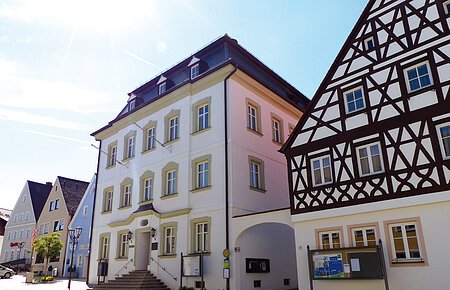 Das Rathaus der Drei-Stämme-Stadt Monheim Straßenansicht der Monheimer Innenstadt: Im Vordergrund das Rathaus der Stadt Monheim, mit weiteren mehreren Gebäuden, darunter ein Fachwerkhaus, das man Schindlerhaus nennt.