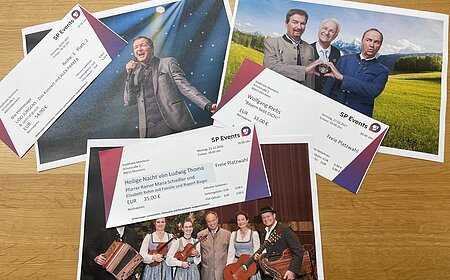 Drei Konzertkarten von SP Events liegen auf Fotos von Musikern in traditioneller und moderner Kleidung auf einem Holztisch. Kartenvorverkauf für die nächsten Veranstaltungen in Monheim