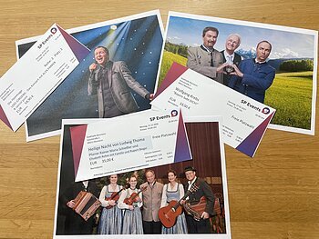 Drei Konzertkarten von SP Events liegen auf Fotos von Musikern in traditioneller und moderner Kleidung auf einem Holztisch. Kartenvorverkauf für die nächsten Veranstaltungen in Monheim