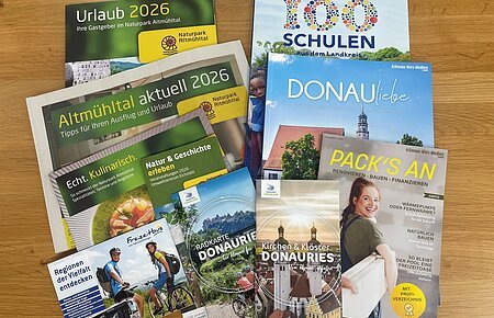 Mehrere Broschüren und Flyer zu Urlaub, Naturpark Altmühltal und Donau-Ries auf Holztisch liegend. Neuauflagen verschiedener Flyer und Broschüren in der Tourist-Information zur Abholung