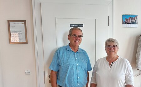 Mann und Frau stehen vor einer weißen Tür in einem Raum mit Holzboden und Pflanzen. Erste Bürgermeisterin Anita Ferber bei der Vereidigung des neuen Feldgeschworenen für den Stadtteil Flotzheim Hermann Färber