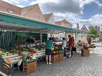 Wochenmarkt Monheim Marktstand des Wochenmarkts in Monheim mit Obst und Gemüse in der Auslage auf dem gepflastertem Marktplatz. Mehrere Personen kaufen dort ein. Fachwerkhäuser im Hintergrund und bewölkter Himmel.