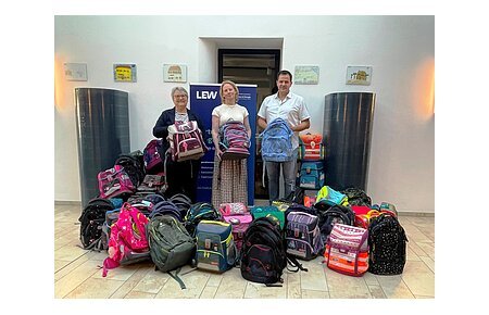 "Ranzen her!" LEW Sammelaktion 2026 in Monheim Drei Personen stehen hinter einer großen Anzahl verschiedener Schulranzen in einem hellen Raum. Die Übergabe der gesammelten Schulranzen in Monheim zur Aktion vom LEW "Ranzen her".