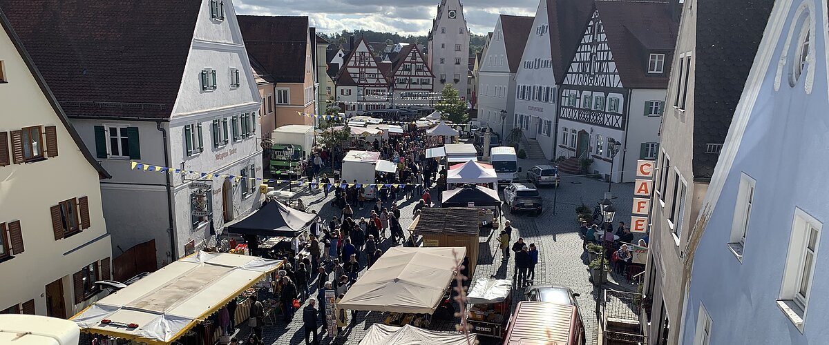 Blick von oben auf belebten Markt mit Ständen und Menschen in einer Altstadt mit Fachwerkhäusern und Café.
